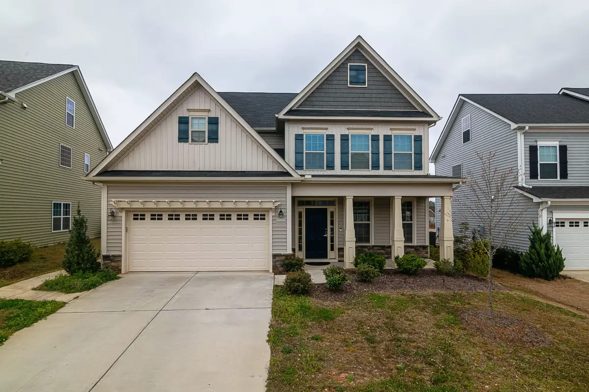 A newer two-story craftsman with board and batten gables, a covered front porch on square columns and a two-car garage.