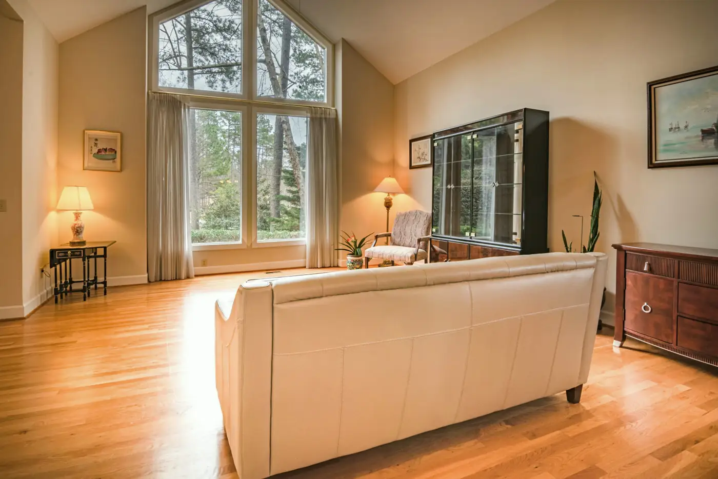 A family room with a vaulted ceiling, tall arched windows, a cream leather sofa and oak floors.