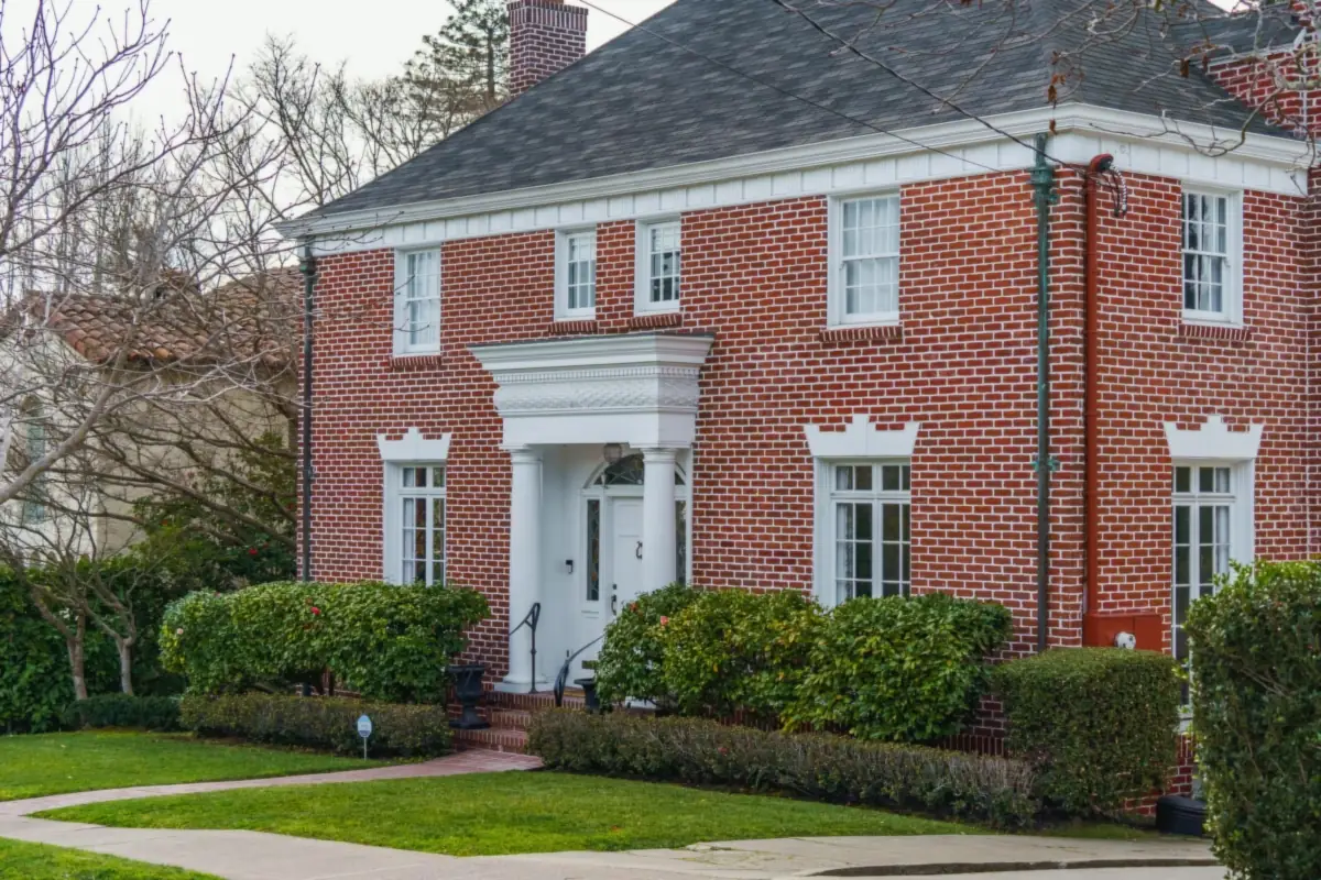 A red brick Georgian house with a white columned portico, white window trim and clipped hedges along the front walk.