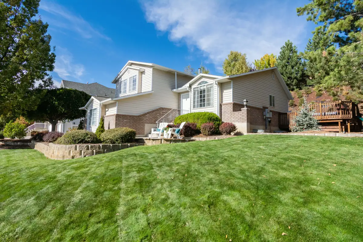 A cream split-level home with brick trim and a raised garden bed, above a broad striped lawn on a clear day.