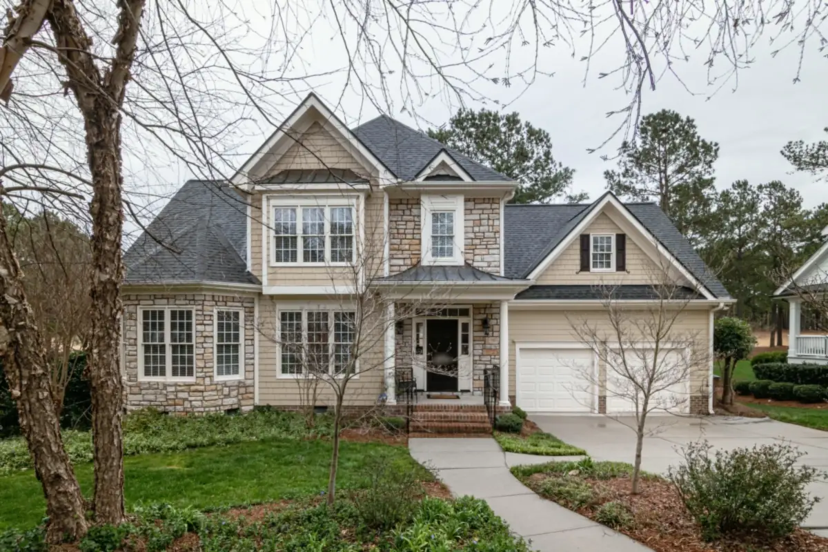 A two-story home with stone and cream shingle siding, a metal-roofed entry and a two-car garage, with a curved front walk.